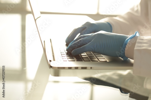 Doctor in blue gloves typing on a laptop in a hospital room