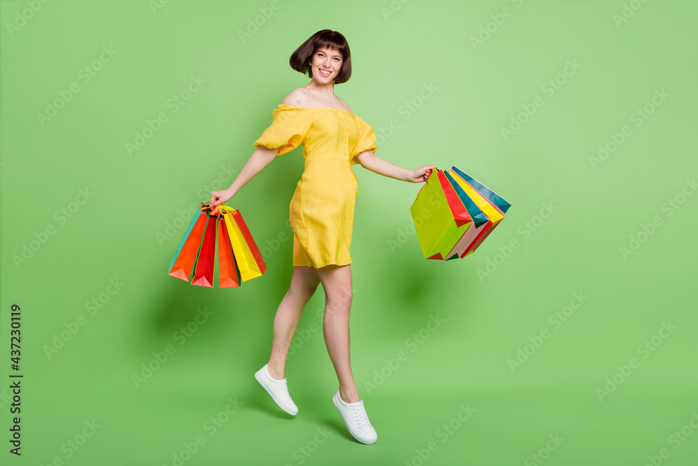 Full length body size view of attractive cheerful girl jumping carrying new clothes isolated over green color background Full length body size view of attractive cheerful girl jumping carrying new clothes isolated over green color background