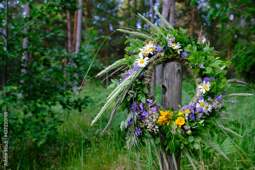 Fototapeta Naklejka Na Ścianę i Meble -  Colorful wreath of flowers, bent and twigs, hung on a wooden pole during the summer solstice festival