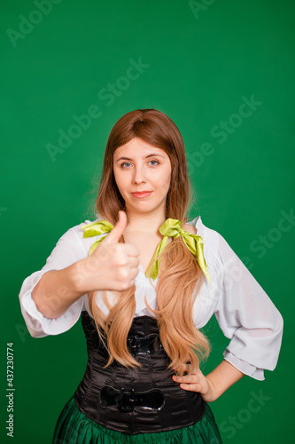 Young woman showing thumb up gesture and smiling isolated on green background. St. Patrick's Day and Oktoberfest celebration concept.
