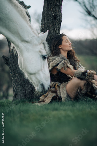 Woman in image of warrior amazon rests under tree near her horse.