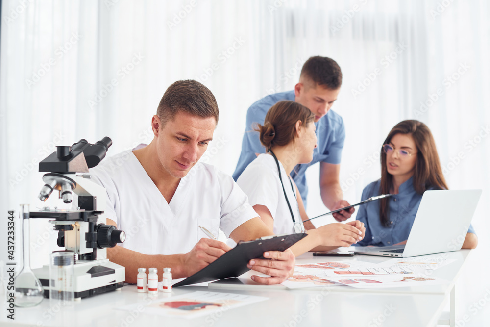 Man with microscope. Group of young doctors is working together in the modern office Man with microscope. Group of young doctors is working together in the modern office