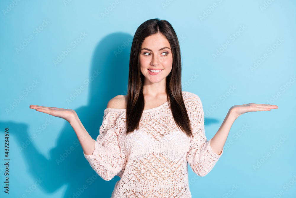 Photo of dreamy cute young woman hold hands empty space look bite teeth isolated on blue color background Photo of dreamy cute young woman hold hands empty space look bite teeth isolated on blue color background