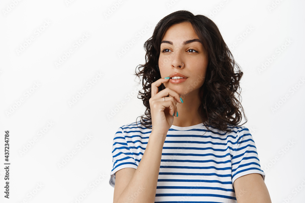 Image of pondering girl looking aside and making choice, touch lip thoughtful, thinking, standing against white background in striped t-shirt Image of pondering girl looking aside and making choice, touch lip thoughtful, thinking, standing against white background in striped t-shirt