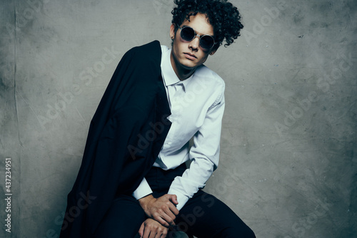 trendy guy with curly hair indoors on a fabric background and a jacket on the shoulder