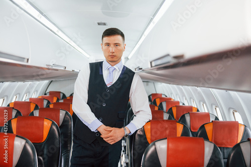 Young steward in uniform on the work in the passanger airplane photo