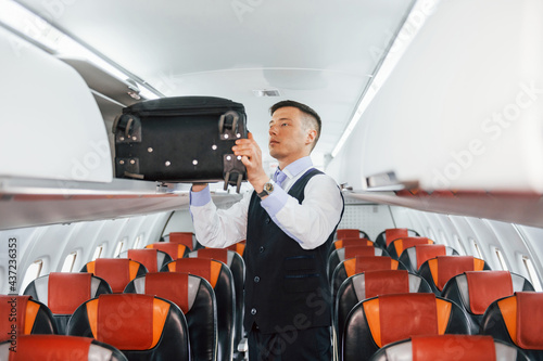 Young steward in uniform on the work in the passanger airplane