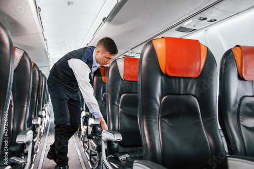 Young steward in uniform on the work in the passanger airplane