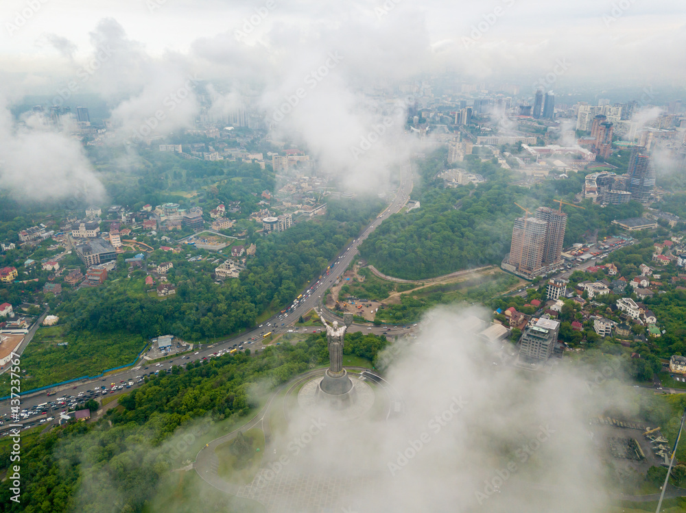 Fototapeta premium Motherland monument in Kiev between the clouds. Aerial drone view.