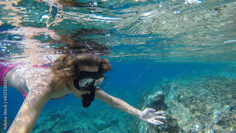 A girl snorkeling and exploring rocky underwater environment and corals.
