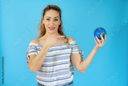 Excited young woman is holding a small Earth globe over blue background.