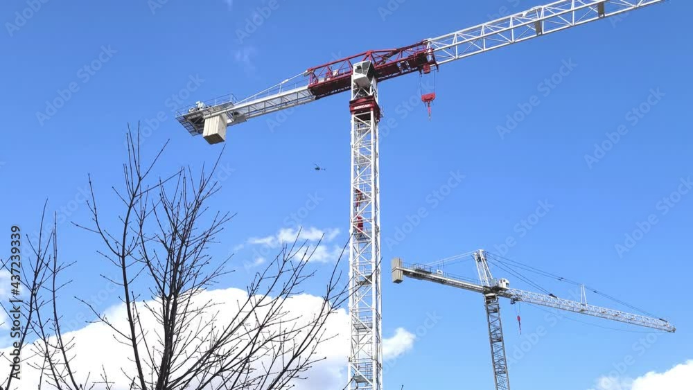 Couple of tall steel construction cranes isolated on blue sky, motion view Couple of tall steel construction cranes isolated on blue sky, motion view