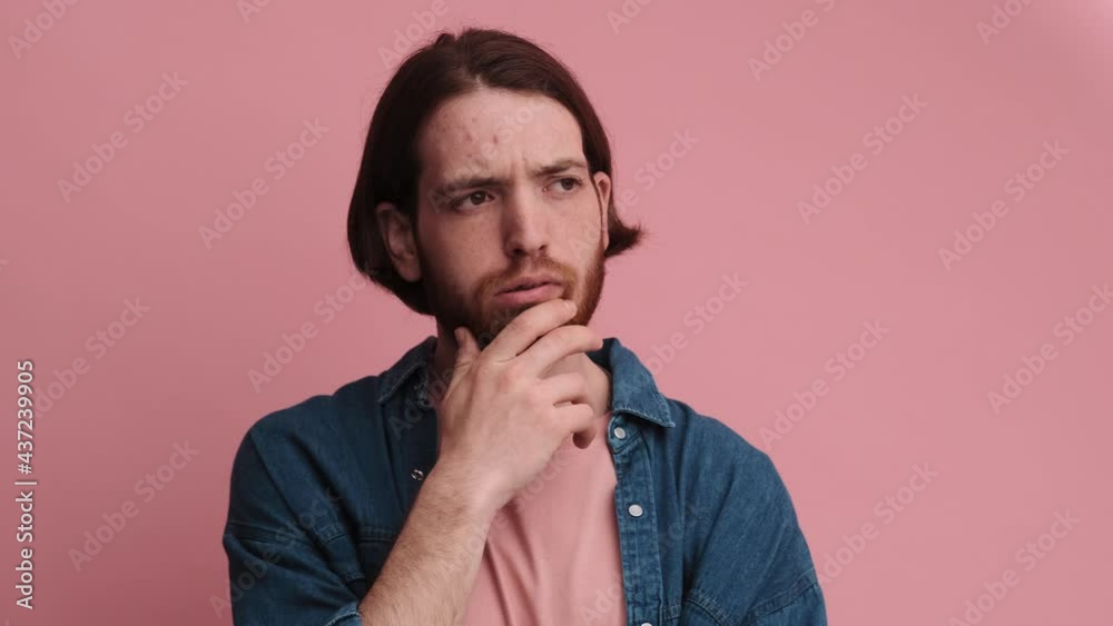 A puzzled man is thinking about something while looking to the camera standing isolated over pink wall in the studio A puzzled man is thinking about something while looking to the camera standing isolated over pink wall in the studio