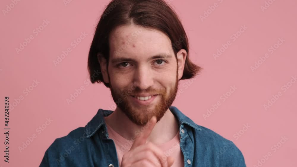 A pleased man is doing secret gesture to the camera isolated on pink color background