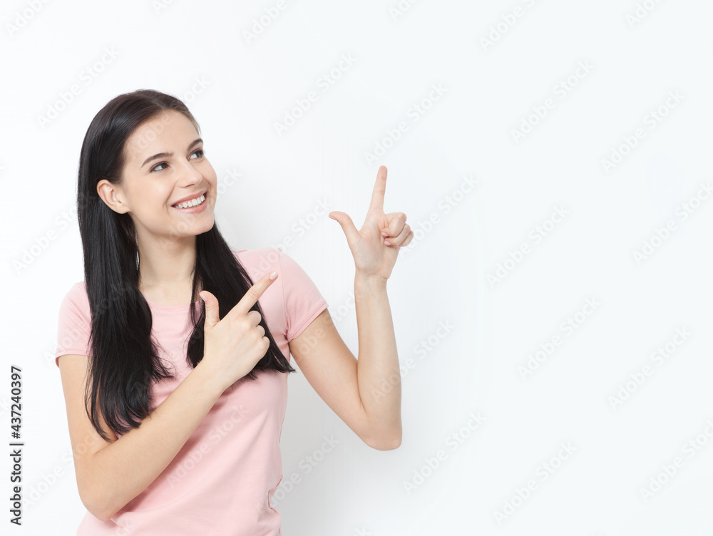 Young woman with white perfect smile in summer clothing shows points fore fingers aside on empty space over white wall. Young woman with white perfect smile in summer clothing shows points fore fingers aside on empty space over white wall.