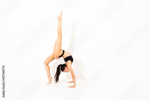 Girl doing stretching in the studio on a white background. A beautiful gymnast with a flexible body and athletic uniform.