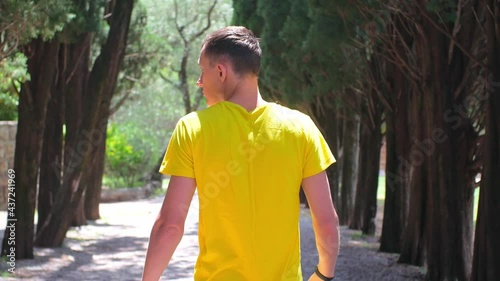 Young attractive man in yellow t-shirt walking through the forest in sunny day