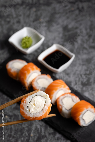 Set of fresh tasty sushi rolls with salmon and cheese. Chopsticks holding sushi on a dark background. Wasabi and soy.
