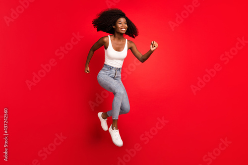 Full body profile side photo of young afro girl happy positive smile jump up go walk run hurry sale isolated over red color background