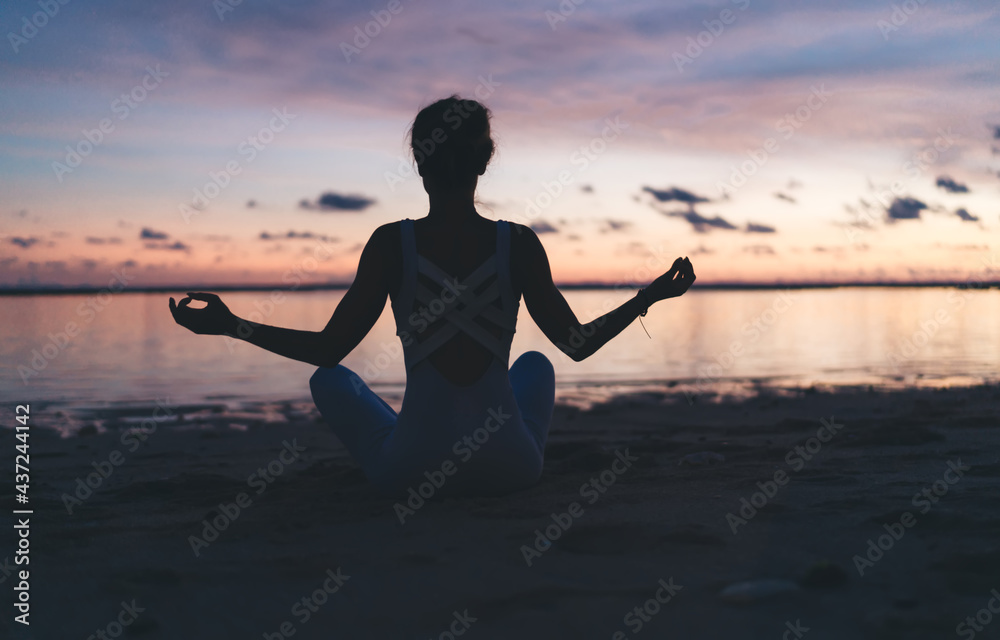 Mental harmony and meditation training during evening yoga at coastline beach, back view of female sitting in lotus pose during aerobic pilates for exercising own body concentration in asana