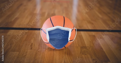 Composition of basketball with face mask on basketball court with copy space