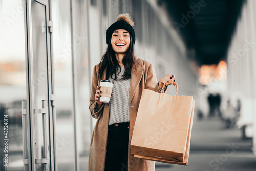 Young woman with shopping bags and coffee walking near mall.