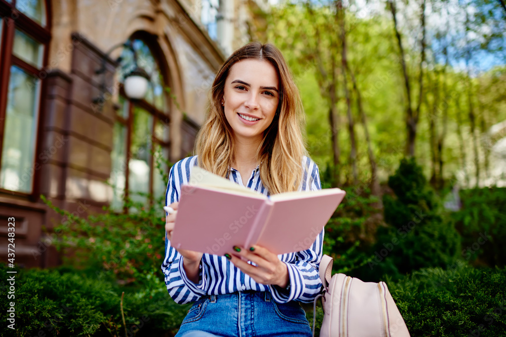 Smiling young woman checking schedule in planner and looking at camera Smiling young woman checking schedule in planner and looking at camera