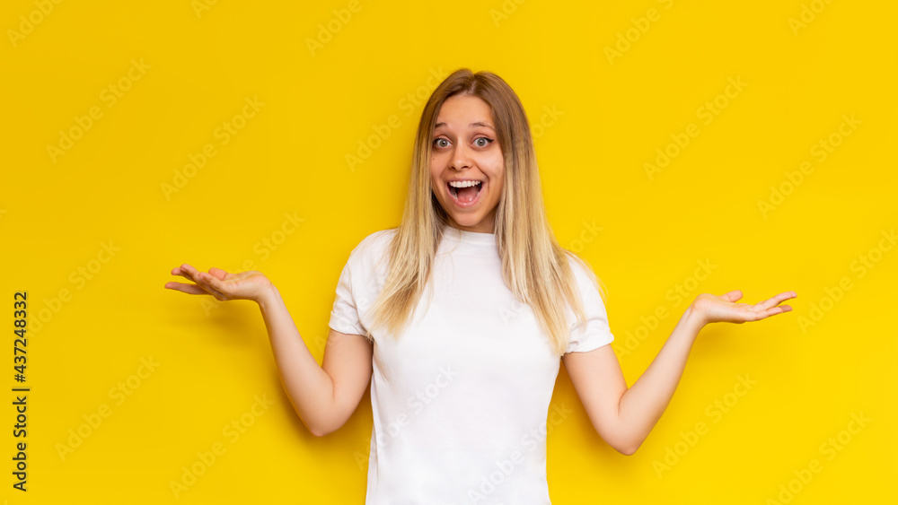 A young caucasian amazed pretty charming blonde woman in a white t-shirt smiles and spreads hands with doubt isolated on a bright color yellow background. Banner A young caucasian amazed pretty charming blonde woman in a white t-shirt smiles and spreads hands with doubt isolated on a bright color yellow background. Banner