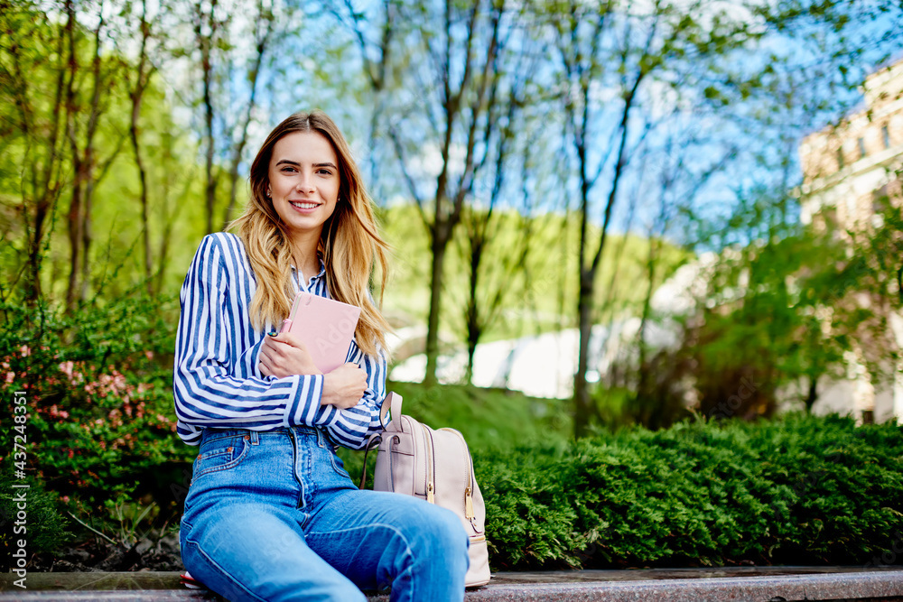 Positive young lady sitting with diary in hands and looking in camera Positive young lady sitting with diary in hands and looking in camera