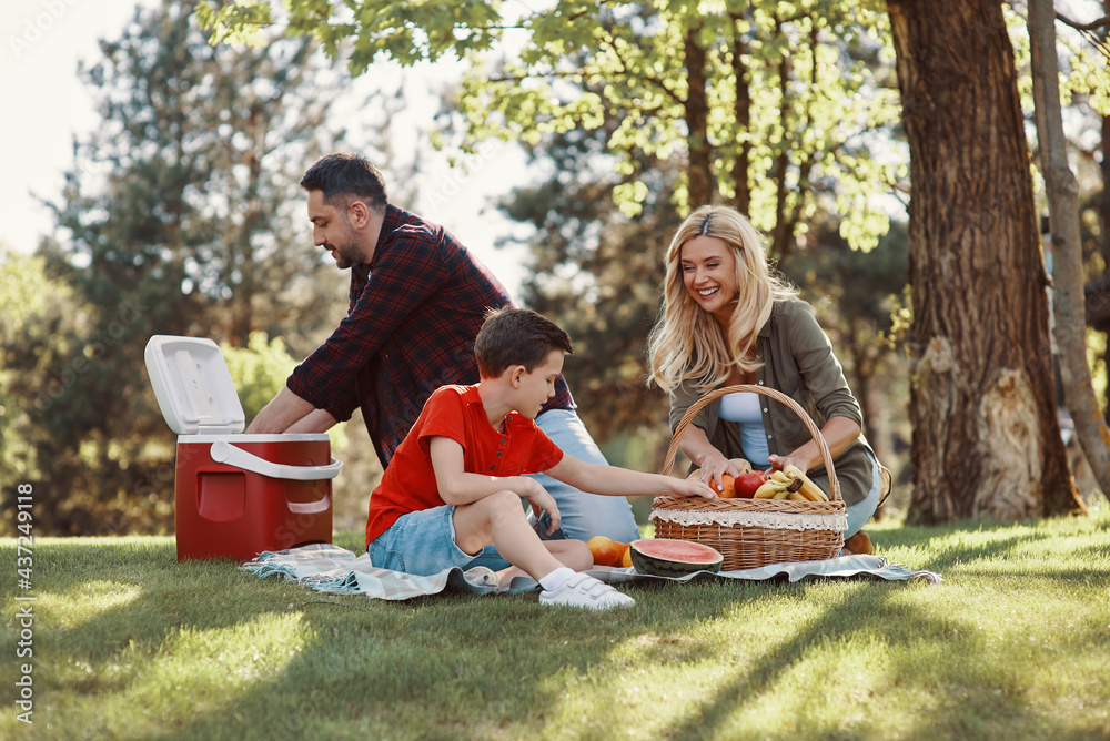 Happy young mother and father with little boy smiling while having picnic outdoors Happy young mother and father with little boy smiling while having picnic outdoors