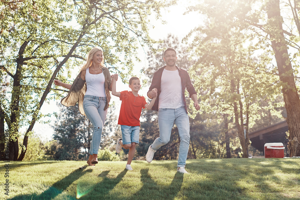 Obraz premium Happy young mother and father with little boy holding hands and walking outdoors