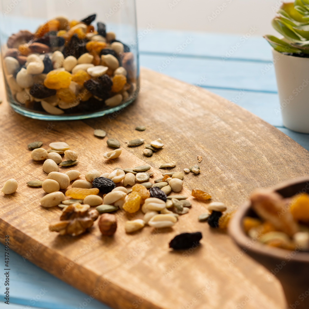 A mixture of loose nuts. Storage of nuts in a glass jar, on a wooden table. Scattered carelessly on the cutting board. Light snack.