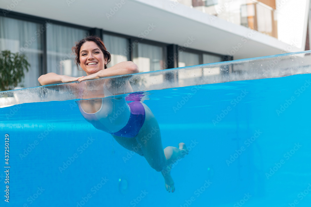 Happy caucasian woman swims in an outdoor pool with a transparent wall in a hotel