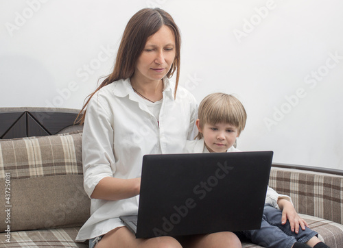  Mom and son are sitting on the couch with a laptop. The concept of remote work.