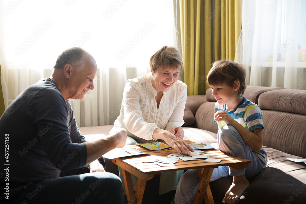 Fototapeta premium grandparents with grandson playing board game together at home. quarantine. Family having fun playing at home. Family board games. 