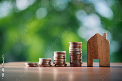 Pile of coins with a wooden house on table financial strategy ideas for real estate investment business.with natural green background.