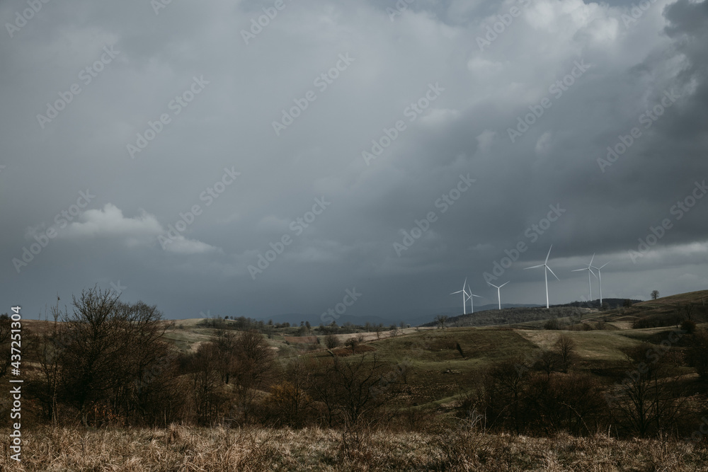 Farm of wind turbines for renewable wind energy on far horizon on hills of Romania under the dark cloudy sky. Copy space.