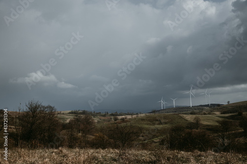 Farm of wind turbines for renewable wind energy on far horizon on hills of Romania under the dark cloudy sky. Copy space.