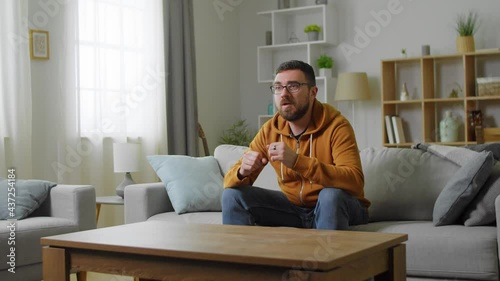 oung male Caucasian sport fan sitting at home on the couch and then cheering up as his team winning.