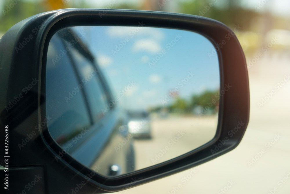 Abstract and blurred view of traffic from behind through the mirrors wing of a black car. 