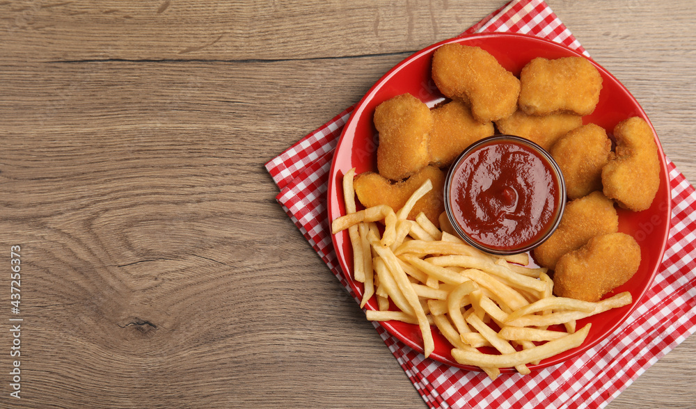 Tasty chicken nuggets and French fries served with ketchup on wooden table, top view. Space for text Tasty chicken nuggets and French fries served with ketchup on wooden table, top view. Space for text
