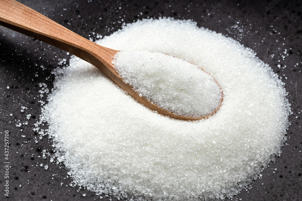 wooden spoon with white refined sugar on black wooden spoon with white refined sugar on black