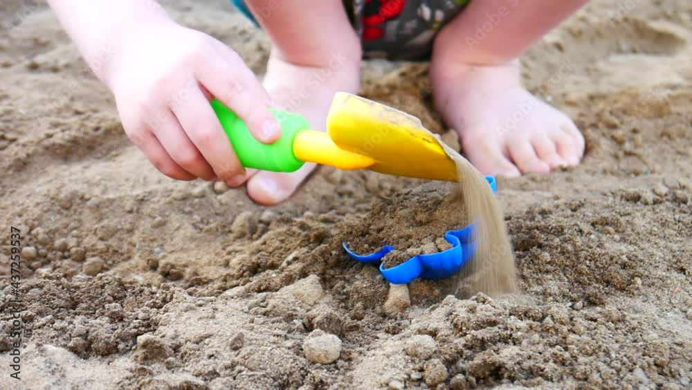 A little boy pours sand on a blue mold playing on the beach A little boy pours sand on a blue mold playing on the beach