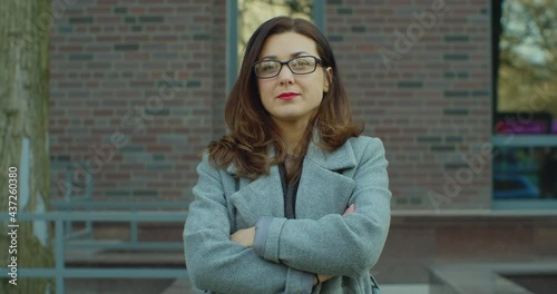 Shot of the beautiful businesswoman in the glasses with hands crossed in front near the big office biuilding. Portrait young businesswoman with glasses standing look at camera smiling near business photo