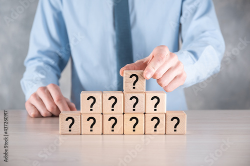 Businessman hold and put wooden cube block shape with question marks on grey table. Space for text.concept for confusion, question or solution