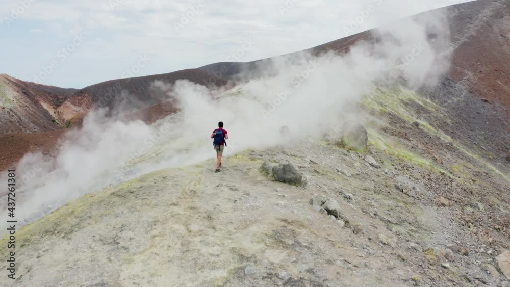 Tracking view of man tourist hiking on volcano and walking trough sulfuric smokes. Volcanic landscape of Volcano Island in Sicily, Aeolian Islands. Aerial follow camera