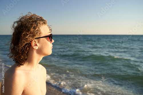 Portrait of a 15 years old teenage boy with curly hair in sunglasses on a beach before sunset. 
