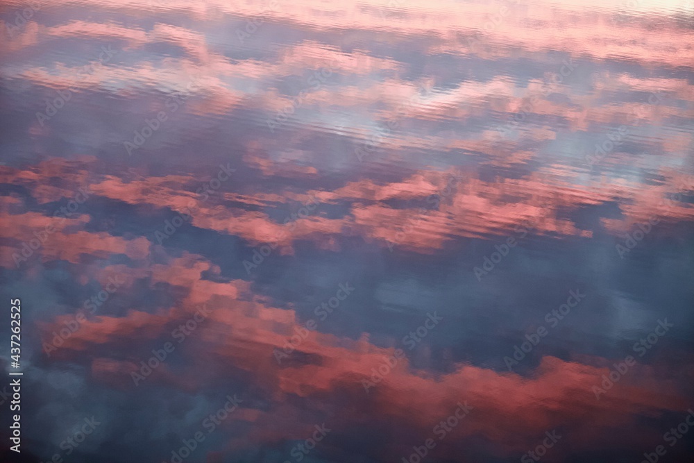 High-contrast shadows and bright reflections on the scarlet surface with purple tints close-up. Ripples on colorful water surface. Abstract backgrounds and textures. Sunset sky reflected in the water.