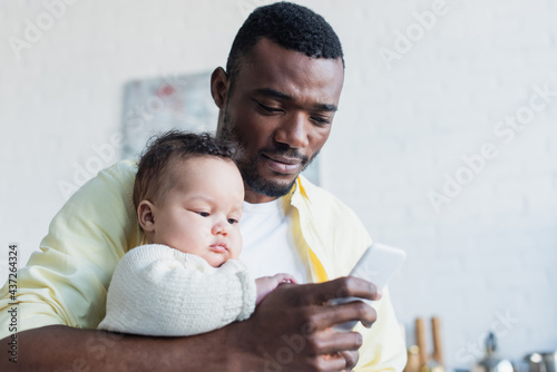african american man holding little daughter while chatting on cellphone