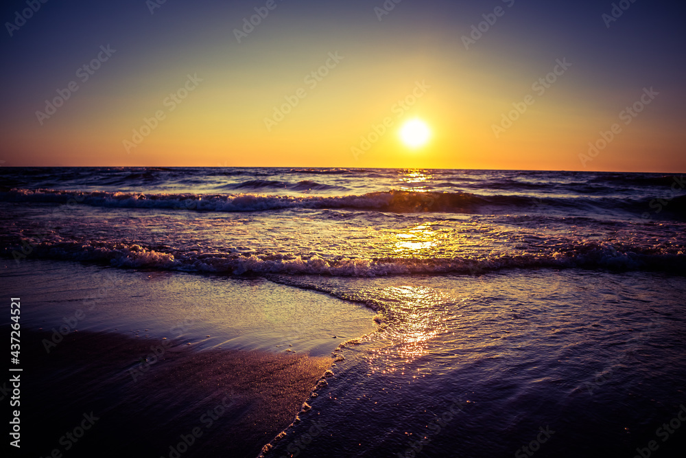 Obraz premium Beautiful small wawes on the sea sand at the beach. Sunset scenery of a Baltic Sea beach. Calm summer evening at seashore.